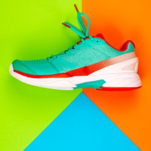 Pickleball court shoes with a teal and red color scheme. The shoes have a flat sole and are designed for quick lateral movement. The laces are tied and the shoes are resting on a colorful backdrop.
